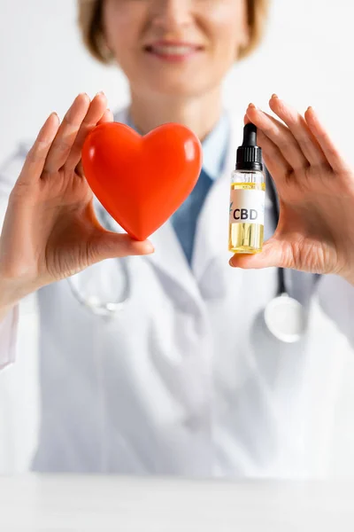 Vue recadrée du médecin heureux et mature tenant bouteille avec lettrage cbd et coeur rouge à la clinique — Photo de stock