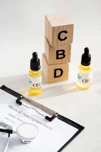 Selective focus of bottles with cbd lettering near wooden cubes and clipboard with medical prescription form — Stock Photo