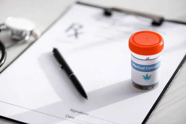 Selective focus of bottle with medical cannabis lettering near pen and clipboard on table — Stock Photo