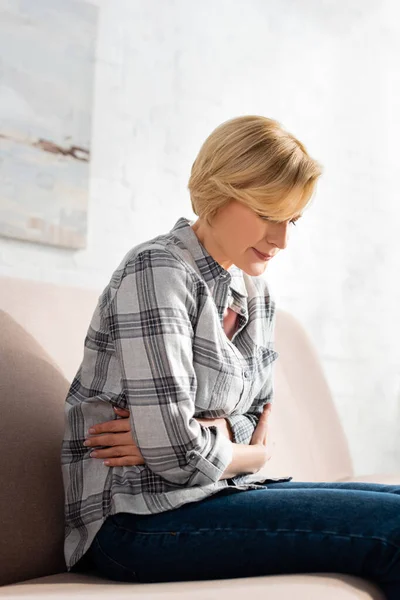 Ältere Frau leidet unter Bauchschmerzen, während sie auf dem Sofa im Wohnzimmer sitzt — Stockfoto