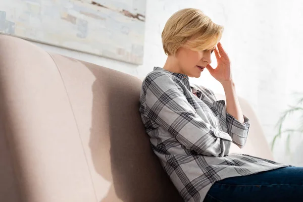 Reife Frau mit Kopfschmerzen sitzt auf Sofa im Wohnzimmer — Stockfoto