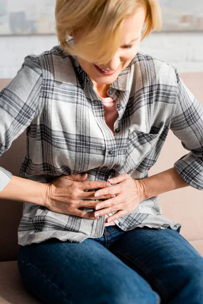 Mature woman suffering from stomach ache and sitting on sofa in living room — Stock Photo