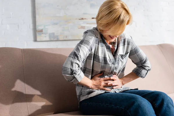 Mature woman suffering from stomach ache while sitting on sofa — Stock Photo