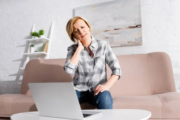 Mature freelancer suffering from neck pain and looking at laptop — Stock Photo