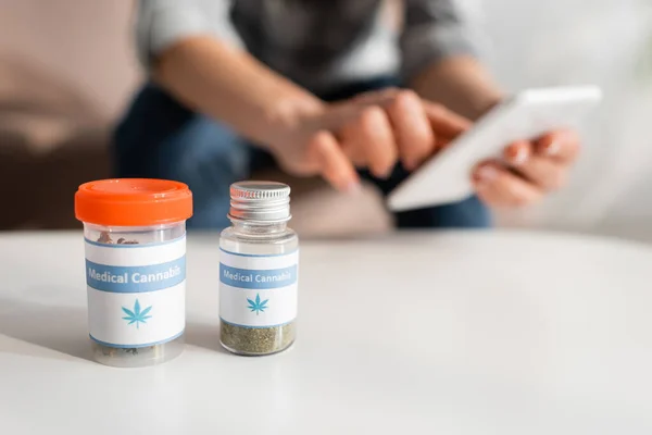 Selective focus of bottles with medical cannabis lettering near mature woman using smartphone — Stock Photo