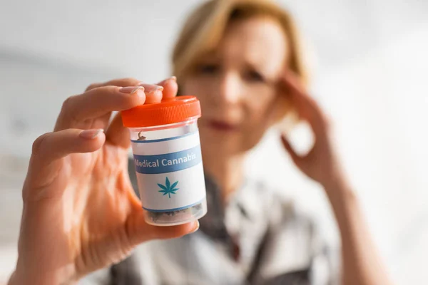 Selective focus of mature woman holding bottle with medical cannabis lettering — Stock Photo