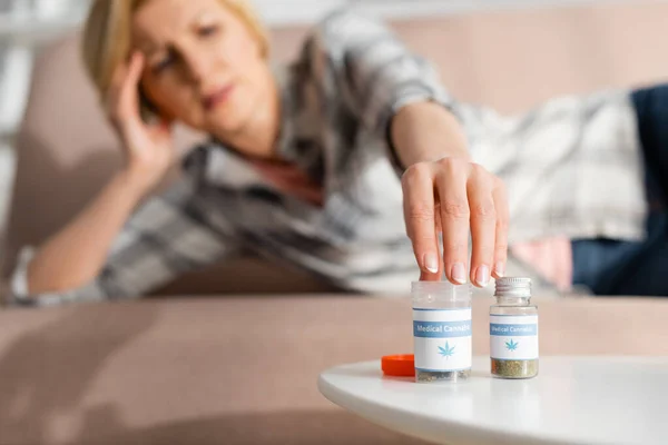 Selektiver Fokus einer reifen Frau, die Flasche mit medizinischem Cannabis-Schriftzug berührt, während sie auf dem Sofa liegt — Stockfoto