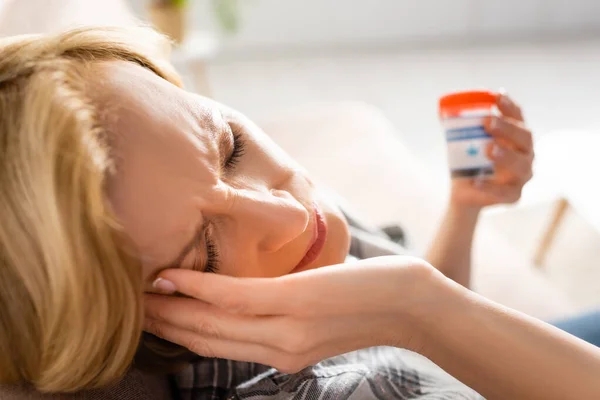 Selective focus of mature woman with migraine holding bottle with medical cannabis lettering — Stock Photo