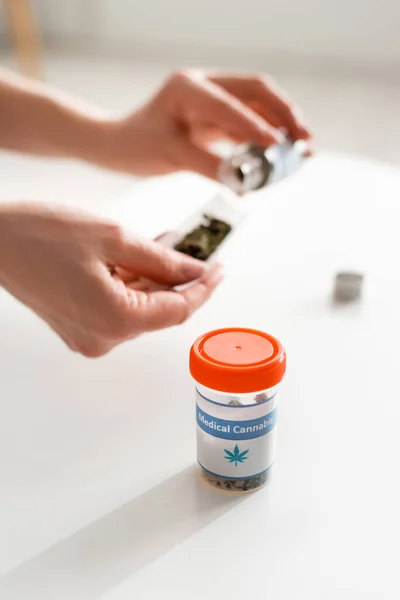 Selective focus of bottle with medical cannabis lettering near mature woman holding paper with dried weed — Stock Photo