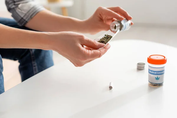 Vista cortada de mulher madura segurando papel perto de garrafa com cannabis medicinal seca — Fotografia de Stock