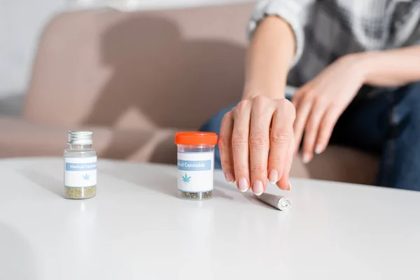 Vista ritagliata della donna matura che prende giunto arrotolato con marijuana essiccata vicino bottiglie con lettering cannabis medica — Foto stock