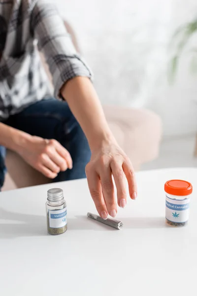 Vista recortada de la mujer madura tomando articulación enrollada con marihuana legal cerca de botellas con letras de cannabis medicinal - foto de stock