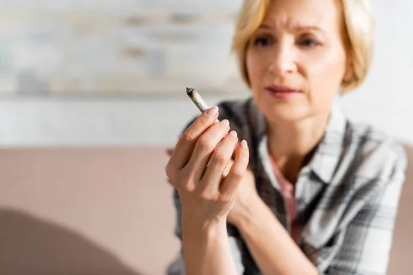 Selective focus of mature woman holding joint with legal marijuana — Stock Photo