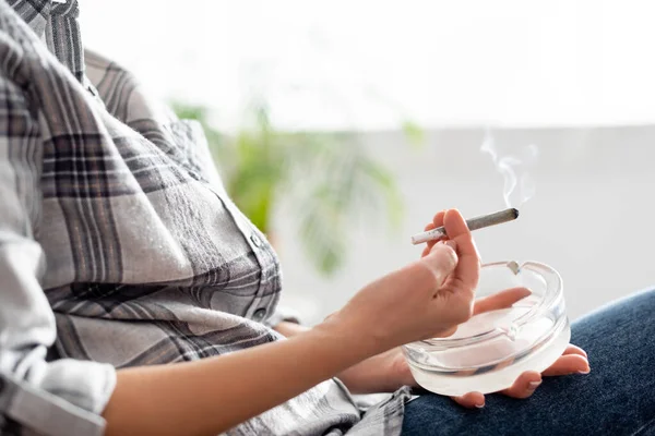 Cropped view of of mature woman holding joint with legal marijuana and ashtray — Stock Photo