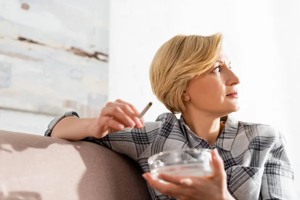 Selective focus of mature woman holding joint with legal marijuana and ashtray — Stock Photo