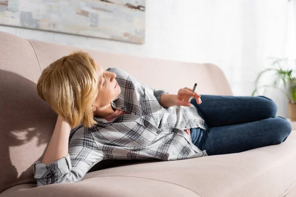 Reife Frau liegt auf Sofa und hält Joint mit legalem Marihuana in der Hand — Stockfoto