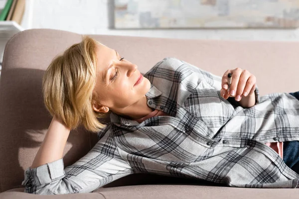 Happy and mature woman lying on sofa and holding joint with legal marijuana — Stock Photo