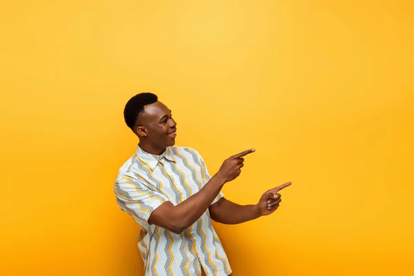 Homem americano africano feliz apontando com os dedos no fundo amarelo — Fotografia de Stock