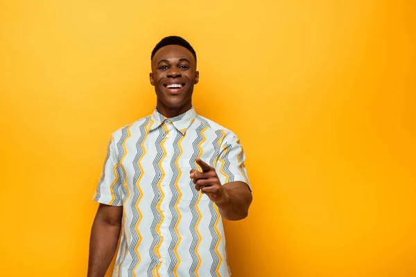 Hombre afroamericano feliz apuntando con el dedo a la cámara sobre fondo amarillo - foto de stock