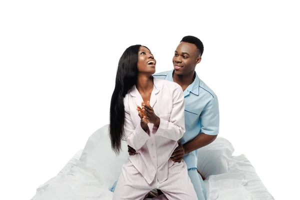 Happy african american couple sitting in bed in pajamas isolated on white — Stock Photo
