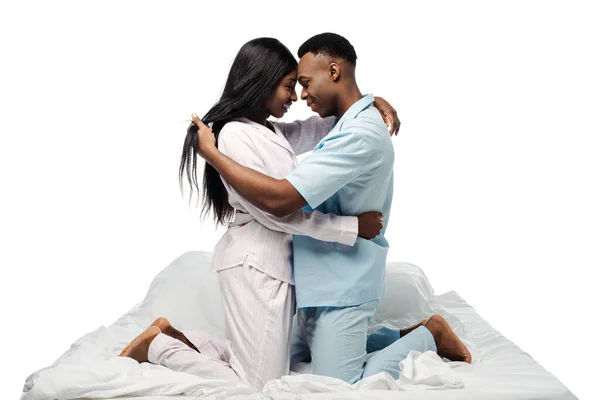 Vue latérale de heureux couple afro-américain embrassant au lit en pyjama isolé sur blanc — Photo de stock