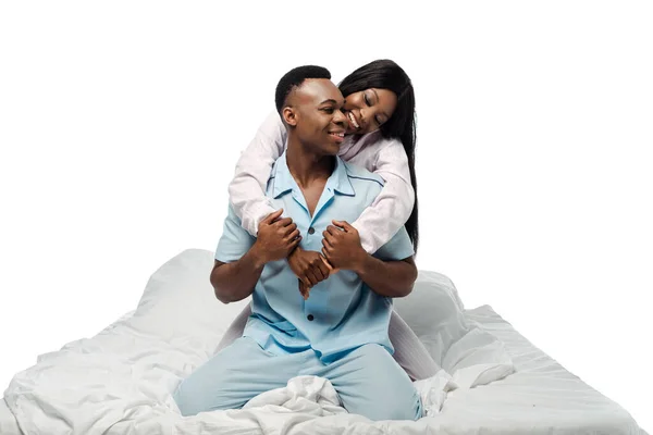 Feliz africano americano pareja abrazándose en cama en pijama aislado en blanco - foto de stock