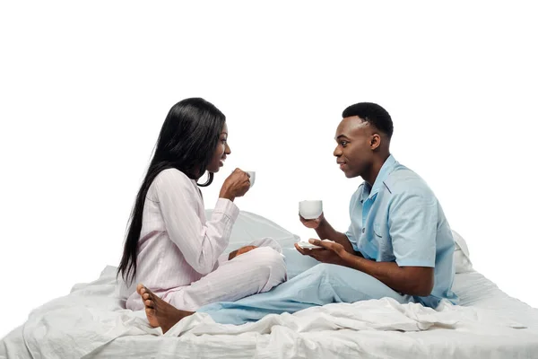 Vue latérale du couple afro-américain buvant du café au lit en pyjama isolé sur blanc — Photo de stock