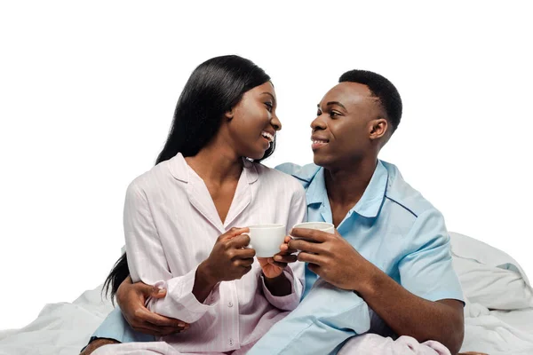 Glücklich afrikanisch-amerikanisches Paar trinkt Kaffee im Bett im Pyjama isoliert auf weiß — Stockfoto