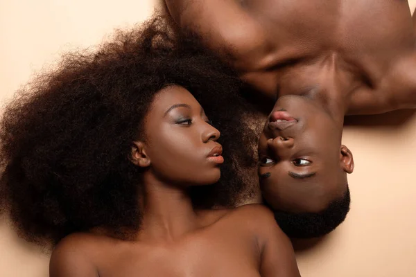 Vista aérea de la sexy pareja afroamericana desnuda acostada en beige - foto de stock