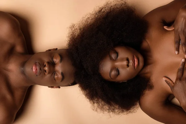 Над головой вид сексуальной обнаженной африканской пары лежащей с закрытыми глазами на бежевый — стоковое фото