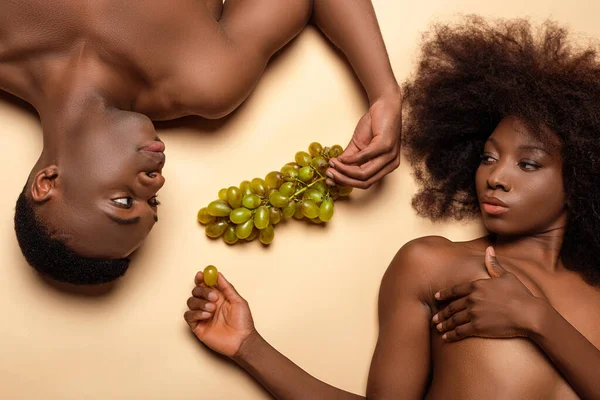 Vista aérea de sexy nu casal afro-americano deitado com uva no bege — Fotografia de Stock