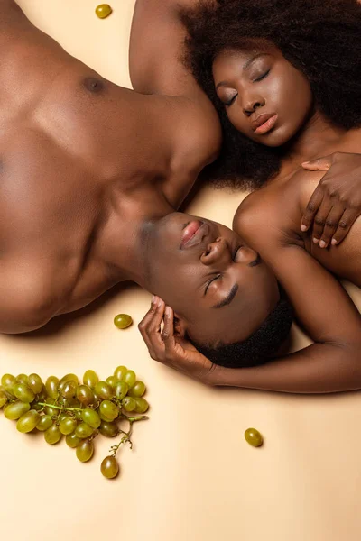 Vista aérea de sexy nu casal afro-americano deitado com uva no bege — Fotografia de Stock
