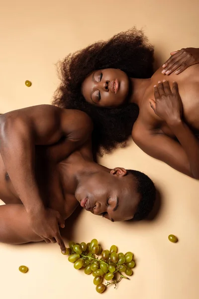 Vista aérea de sexy nu casal afro-americano deitado com uva no bege — Fotografia de Stock