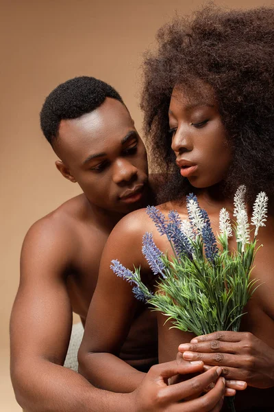 Sexy desnudo africano americano pareja posando con planta en beige - foto de stock