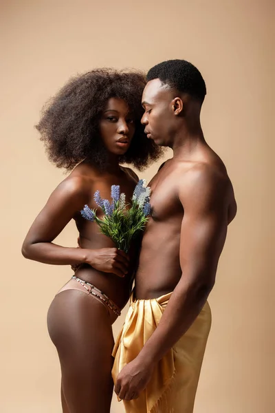 Vista lateral de la sexy pareja afroamericana desnuda posando con planta aislada en beige - foto de stock