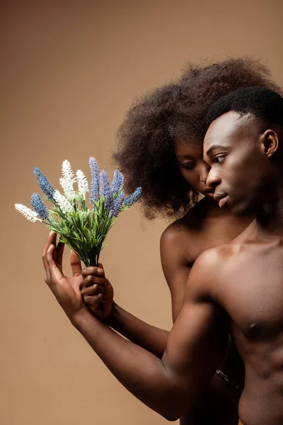Sexy desnudo africano americano pareja posando con planta en beige - foto de stock