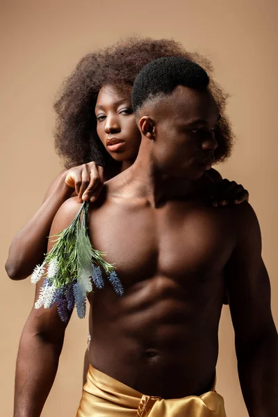 Sexy desnudo africano americano pareja posando con planta aislado en beige - foto de stock