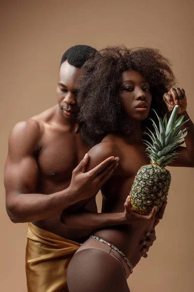 Sexy naked african american couple posing with pineapple on beige — Stock Photo