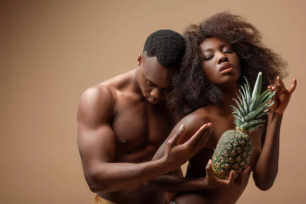 Sexy naked african american couple posing with pineapple on beige — Stock Photo