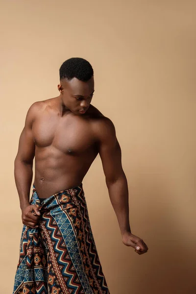 Sexy desnudo tribal afro hombre cubierto en manta posando en beige - foto de stock
