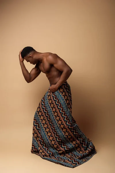 Sexy naked tribal afro man covered in blanket posing on beige — Stock Photo