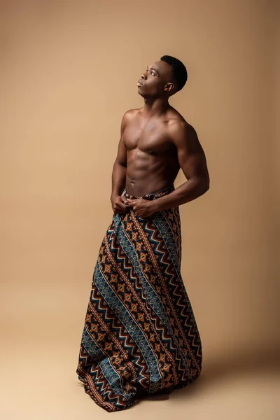 Sexy naked tribal afro man covered in blanket posing on beige — Stock Photo