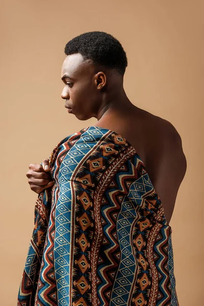 Sexy naked tribal afro man covered in blanket posing isolated on beige — Stock Photo