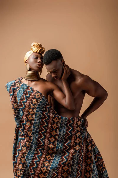 Sexy nu tribal afro femme recouvert de couverture posant près de l'homme sur beige — Photo de stock