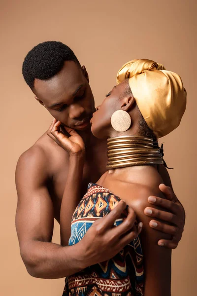 Sexy desnudo tribal afro mujer cubierto en manta besos hombre aislado en beige - foto de stock