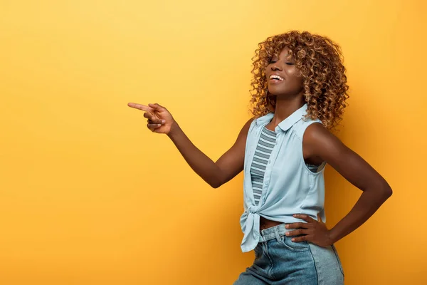 Happy african american woman pointing with finger on yellow background — Stock Photo