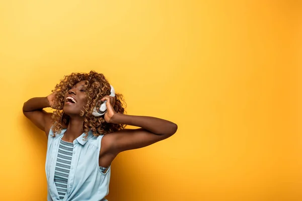 Mujer afroamericana feliz escuchando música en auriculares sobre fondo amarillo - foto de stock
