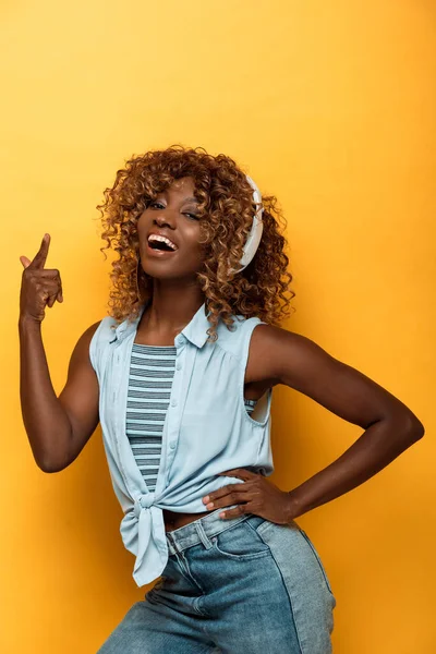 Щаслива афроамериканка слухає музику в навушниках на жовтому фоні — стокове фото