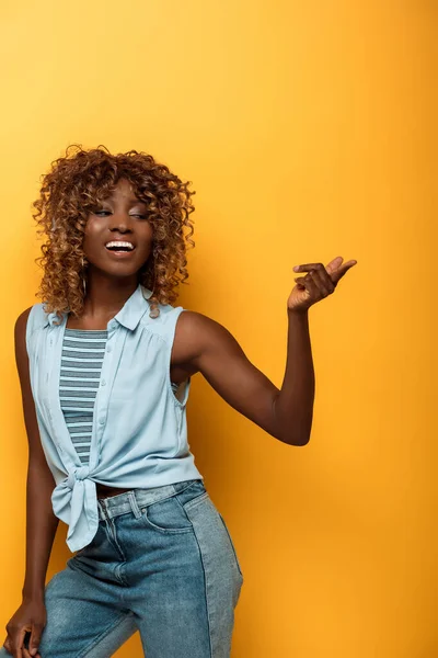 Happy african american woman pointing with finger on yellow background — Stock Photo