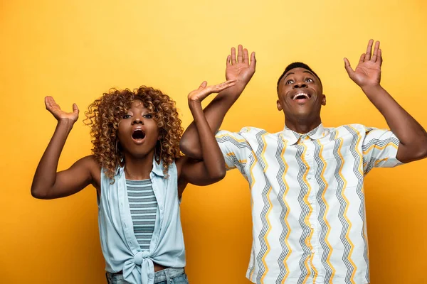 Shocked african american couple with open mouths gesturing on yellow colorful background — Stock Photo